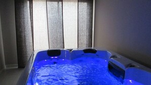 A hot tub with blue lighting, a window with blinds, and a tiled floor.