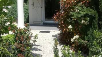 Un espace extérieur abrité, doté d’un chemin de gravier menant à une porte, et entouré de divers arbustes et plantes.