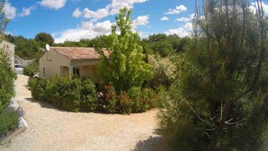 A house with a gravel driveway, surrounded by dense vegetation and trees.