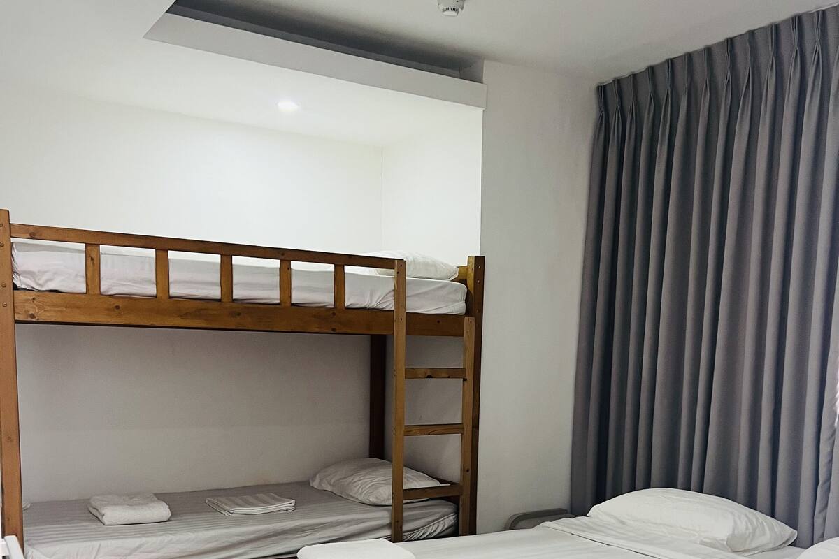 Ein Zimmer mit Etagenbett, einem Einzelbett und einem Vorhang.