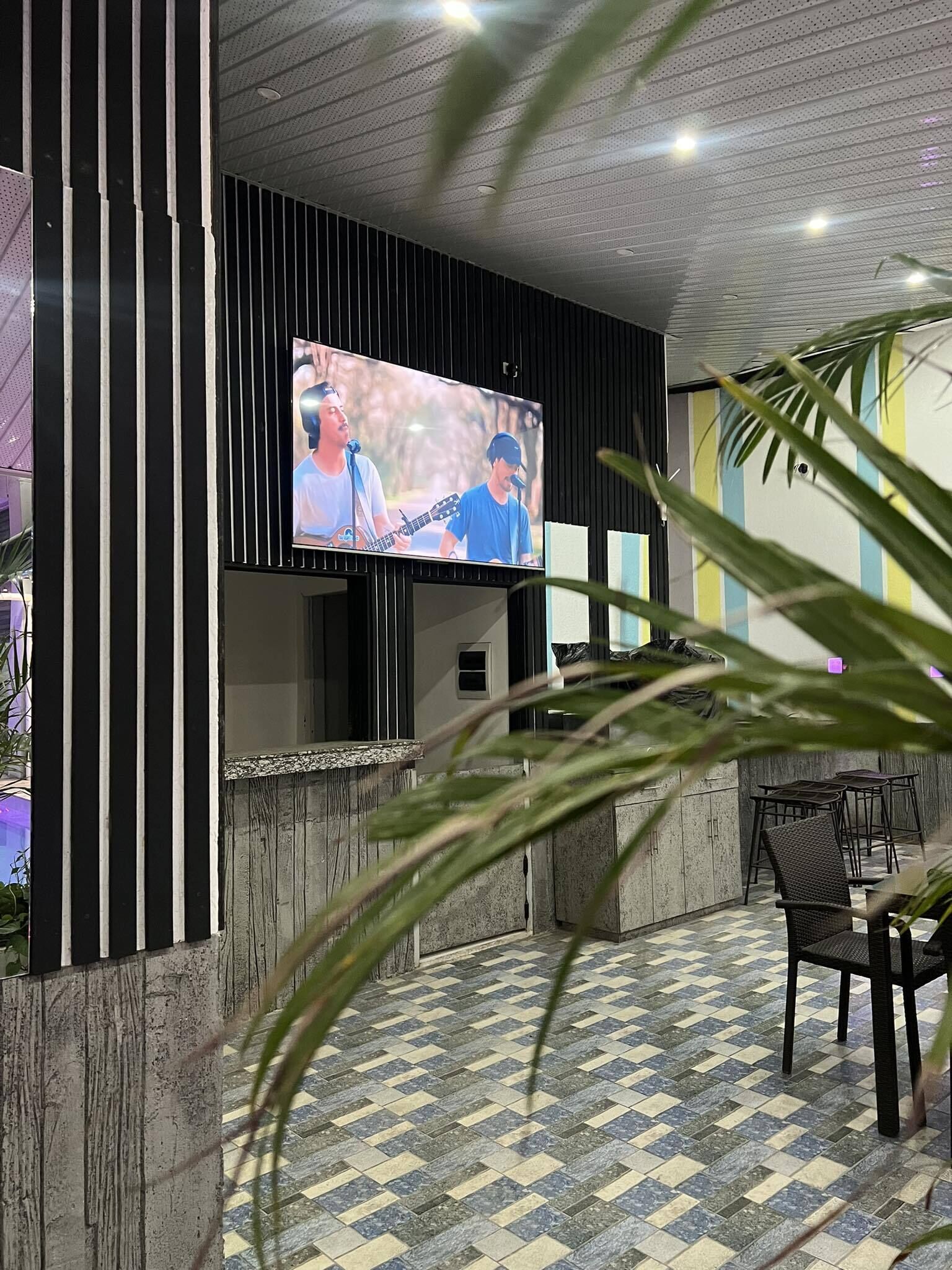 Uma área de recepção com televisão na parede, balcão de check-in e um espaço de estar com cadeiras e uma mesa.