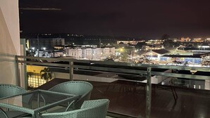 Un balcón con sillones de mimbre y una mesa, con vistas a un paisaje urbano nocturno.