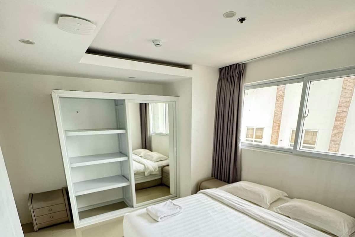 Ein modernes Schlafzimmer mit einem großen Bett, einem begehbaren Kleiderschrank und einem Fenster mit Blick auf Gebäude.