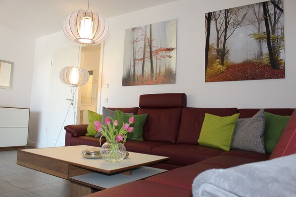 Un salon moderne avec un canapé rouge, une table basse et un tableau représentant une scène de forêt.