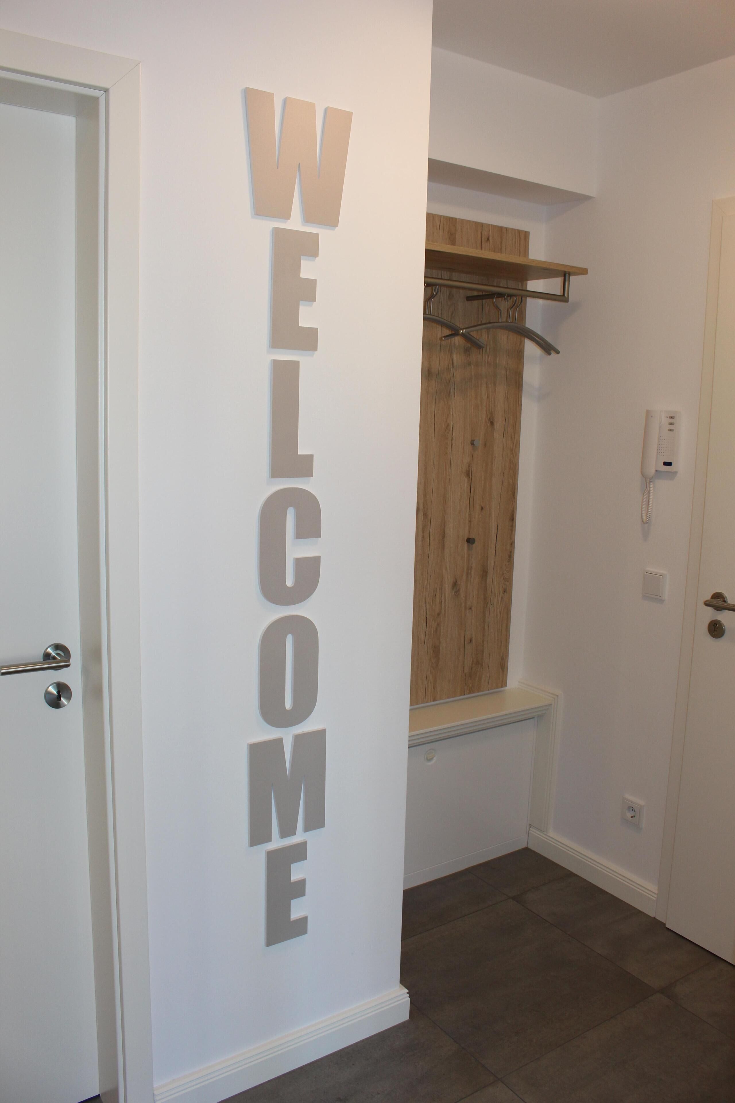 Un pasillo con un cartel que dice 'WELCOME', un banco de madera y un perchero.