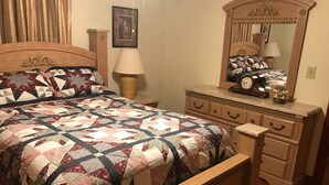 A bedroom with a wooden bed, a nightstand, a dresser, a mirror, and a clock.