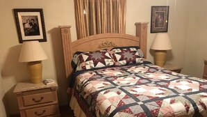 A bedroom with a wooden bed, a nightstand with a lamp, a dresser with drawers, and two framed pictures on the wall.