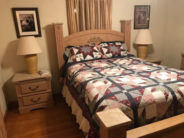 A bedroom with a wooden bed, a nightstand with a lamp, a dresser with drawers, and two framed pictures on the wall.