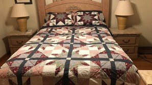 A bed with a quilt, two bedside tables with lamps, and framed pictures on the wall.
