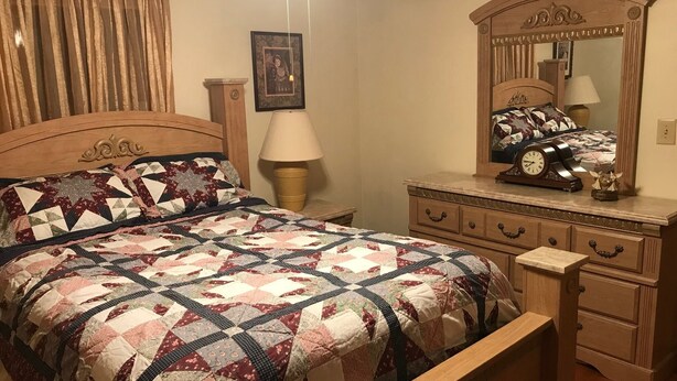 A bedroom with a wooden bed, a dresser with a mirror, and a nightstand with a lamp.