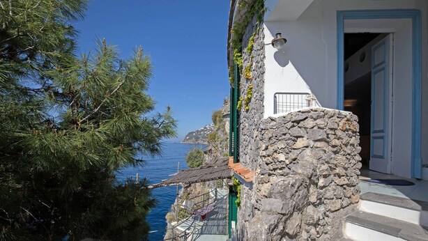 Un edificio costiero con una scala in pietra, vista sul mare e una porta con davanzali blu.