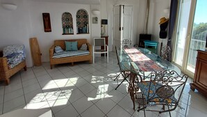 Una stanza luminosa con una tavola da pranzo in vetro, un divano in vimini e vista sull'esterno.