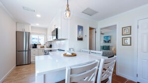 Una cocina moderna con armarios blancos, un refrigerador de acero inoxidable, una isla grande con sillas e iluminación colgante.