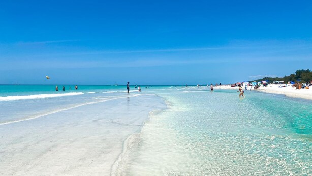 Una playa con agua turquesa cristalina, orilla de arena y sombrillas.