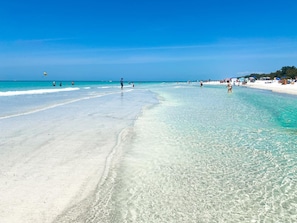 A beach with clear turquoise water, sandy shore, and umbrellas.