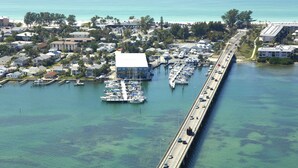 Una marina con barcos amarrados, un puente y un pueblo costero con edificios y árboles.