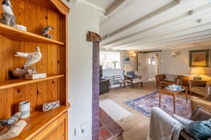 A cozy living room with wooden shelves, a fireplace, and comfortable seating. - Church Cottage, Thornham, Norfolk (Hunstanton)