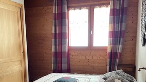 Una camera da letto in legno con un letto, tende a quadri e una finestra.
