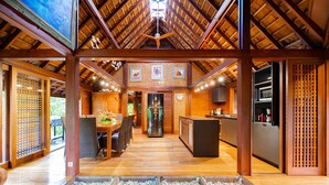 A spacious kitchen with wooden beams, a dining area with wicker chairs, and a refrigerator.