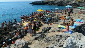 Ein felsiger Strand mit badenden und sonnenbächelnden Personen.