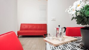 A modern room with a red sofa, a wooden table with a coffee maker and glasses, and a potted plant. - Ampio alloggio con due camere da letto (Verona)