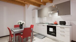 A modern kitchen with white cabinets, a gas stove, a microwave, and a dining area with a table and red chairs. - Ampio alloggio con due camere da letto (Verona)