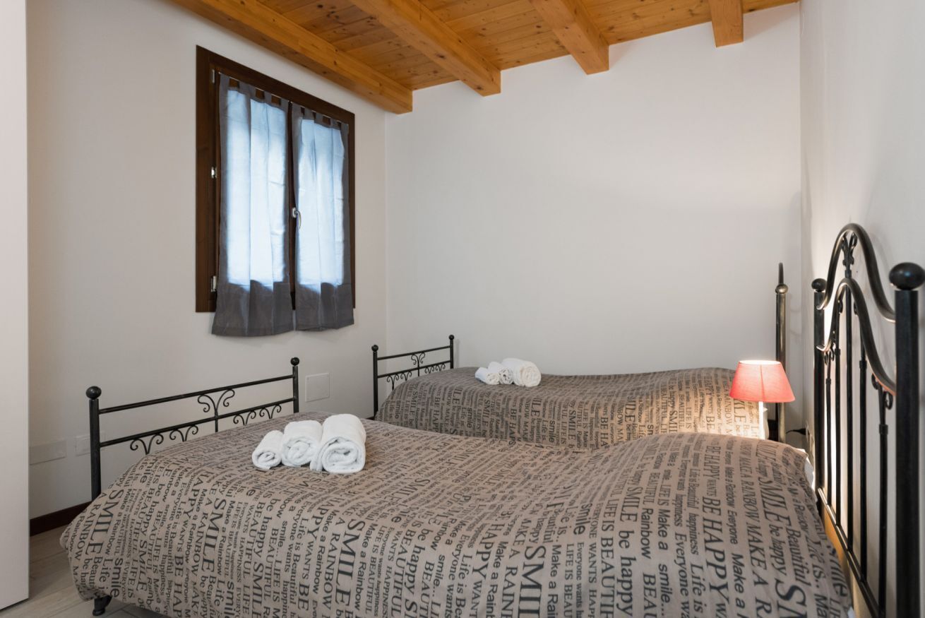 Un dormitorio con dos camas, una ventana con cortinas, una lámpara de noche y toallas sobre las camas.