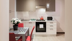 A modern kitchen with white cabinets, a gas stove, a microwave, and a sink. There is a dining table with red chairs and a potted plant. - Ampio alloggio con due camere da letto (Verona)