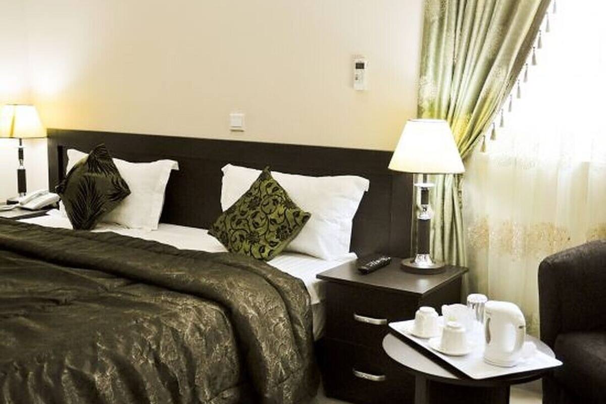A hotel room with a bed, bedside tables, lamps, a chair, and a window with curtains.