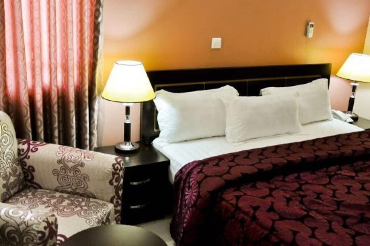 A hotel room with a bed, two bedside lamps, a chair, and a nightstand.