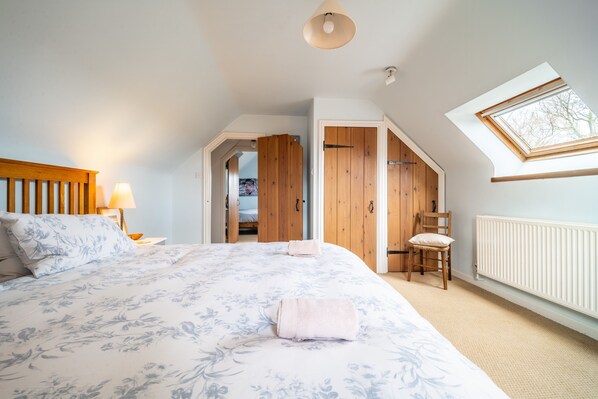 Een slaapkamer met een groot bed, dakraam, een houten kledingkast en een stoel.