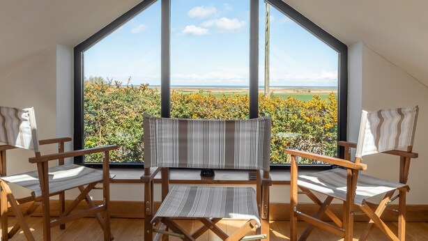 Une pièce dotée d’une grande fenêtre, de chaises en bois et offrant une vue sur un champ et le ciel.