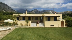 Uma casa moderna de dois andares com telhado plano, varanda frontal e um pequeno jardim.