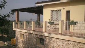 Un immeuble de deux étages avec une façade en pierre, un balcon doté de rampes en métal et une fenêtre munie d’une grille de sécurité.