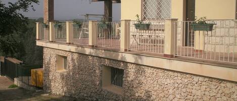 A two-story building with a stone facade, a balcony with metal railings, and a window with a security screen.