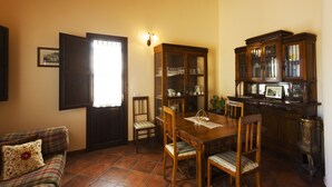 Un coin repas avec une table et des chaises en bois, un meuble avec des portes en verre et un canapé agrémenté d’un coussin à motifs floraux.