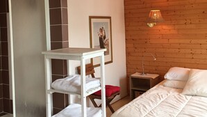 Une chambre avec un plafond en bois, un lit avec une literie blanche, une étagère blanche avec des serviettes, un tableau encadré au mur et une petite table avec une lampe.