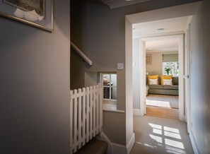 A hallway with a white picket fence, a staircase, and a view into a living room with a sofa and cushions.