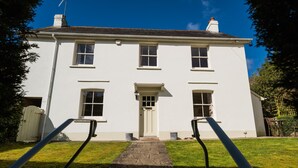 A two-story white building with a central entrance, a small porch, and a stone pathway leading to the door.
