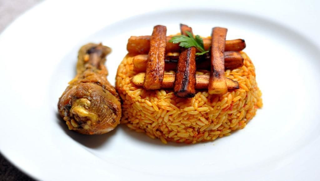 A plate with a piece of meat and a mound of rice topped with grilled vegetables.