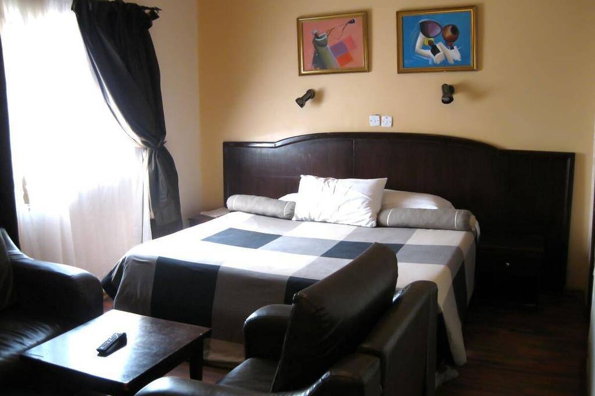 A hotel room with a bed, two chairs, a small table, and two paintings on the wall.