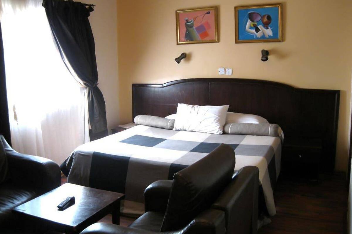 A hotel room with a bed, two paintings, a desk, and a chair.