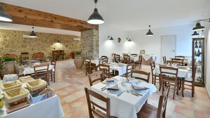 Un espace repas avec plusieurs tables dressées pour les repas, des chaises en bois et des lampes suspendues.