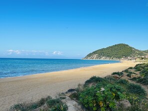Uma praia com areal, uma pequena colina com vegetação e um céu azul límpido.