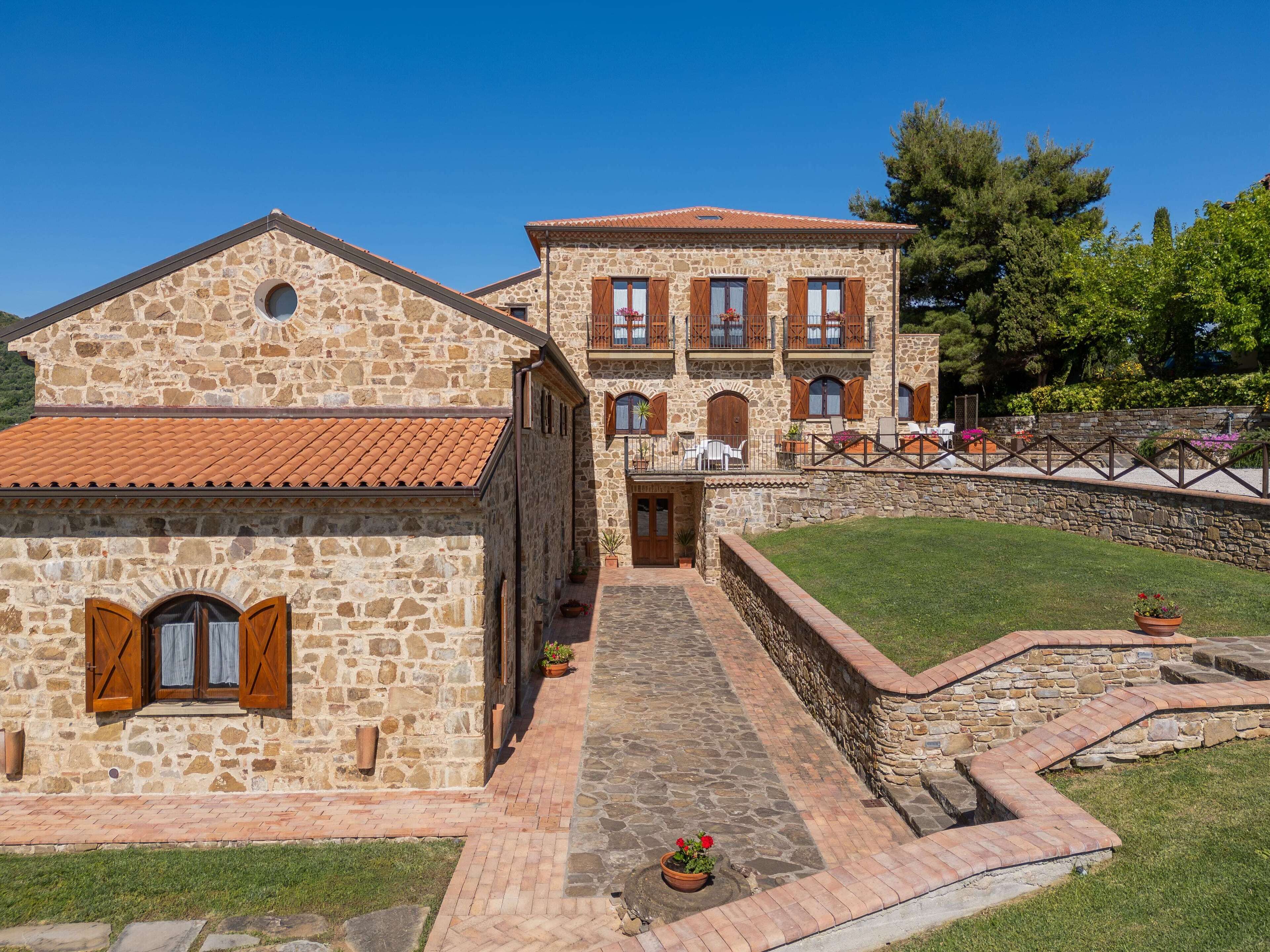 A stone building with a tiled roof, a stone pathway leading to the entrance, and a small garden area with potted plants.