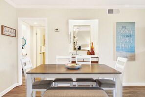 A dining area with a wooden table, white chairs, and a bowl of food. There are wall decorations and a mirror above the table.