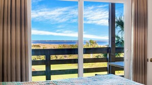 Een kamer met een grote schuifglazen deur die uitkomt op een balkon met uitzicht op een strand en een verafgelegen landschap.