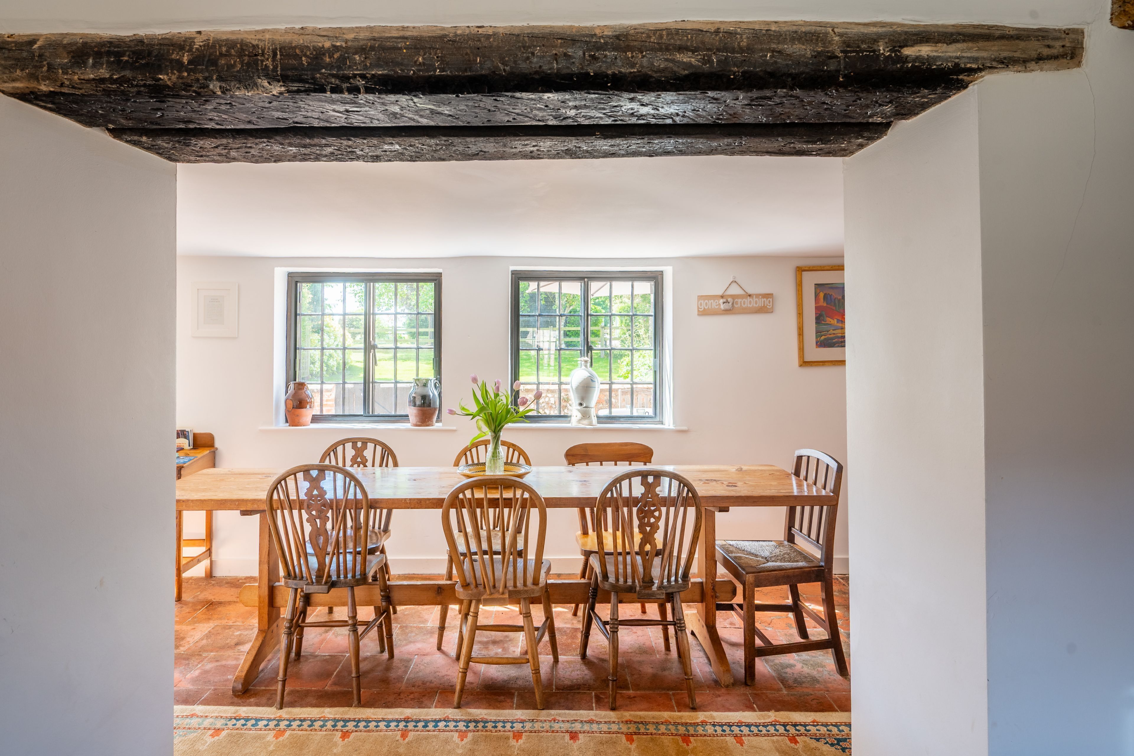A dining area with a wooden table and chairs, two windows, and a rustic ceiling.