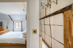 A bedroom with a wooden headboard, a bed, a nightstand, a dresser, a television, and a window with curtains.