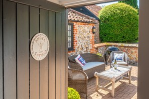 A cozy outdoor seating area with wicker furniture, a stone wall, and a sign reading 'Angel Cottage.'